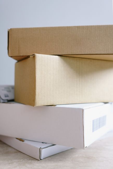 The image shows three stacked cardboard boxes, with the top box being plain brown kraft paper, the middle box a slightly lighter shade of brown, and the bottom box white with a barcode label visible. 